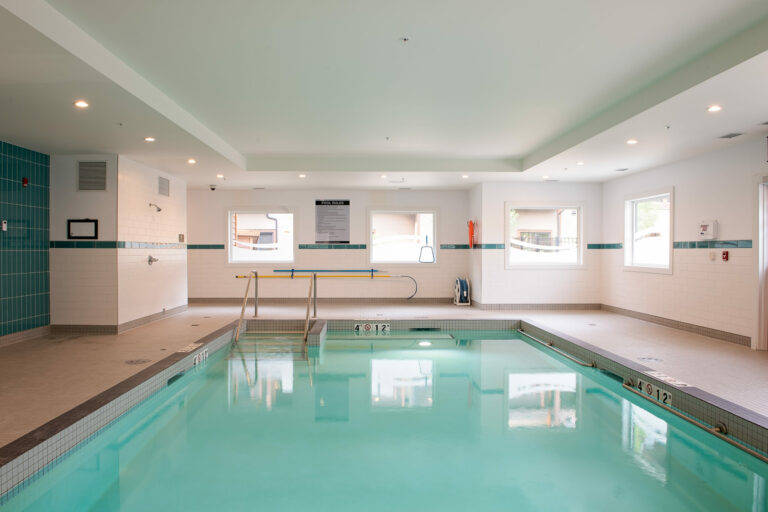 A bright blue indoor pool with sunlit windows and white and turquoise tiles in Origin at Spring Creek's spa facilities.